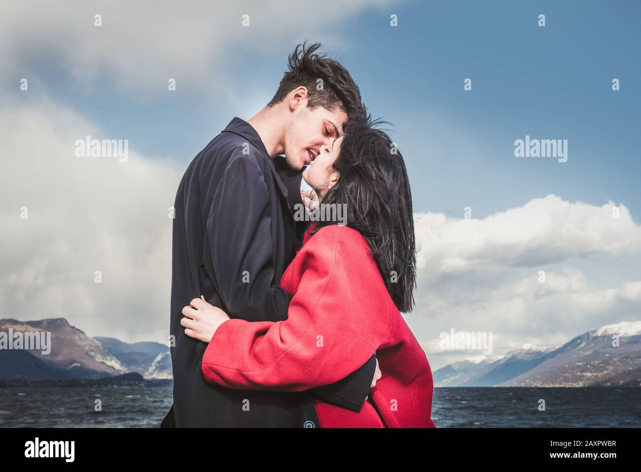 Loving couples, kiss on the background of the lake and mountains. Kissing brunette man and brown-haired woman outdoors Stock Photo
