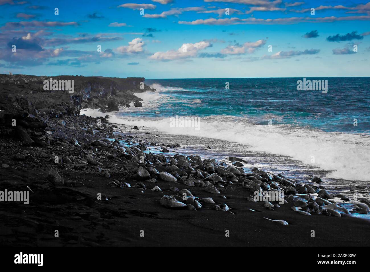 Waves breaking onto a beach of volcanic rock. Stock Photo
