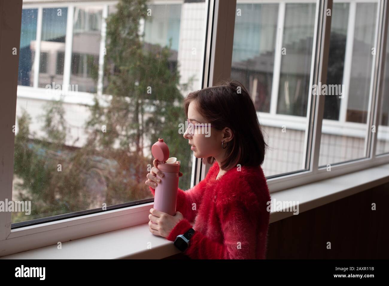 girl with cup. schoolgirl girl in glasses drinks water from a thermomug.A schoolgirl drinks tea, juice or water from a thermal cup or thermos. girl at Stock Photo