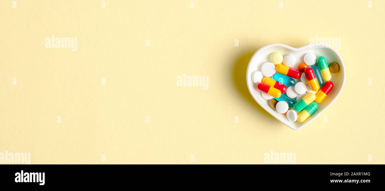 Heart shaped plate with colorful medical pills in capsule on yellow background. Top view with copy space. Healthcare, pharmacy, medicine concept. Medi Stock Photo
