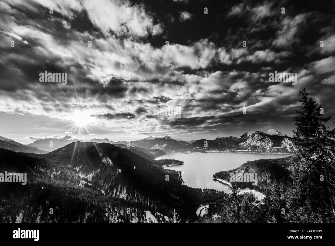 Sun star over the Zugspitze and the lake Walchensee, with Herzogstand, Heimgarten and Simetsberg in the foreground as black and white picture Stock Photo
