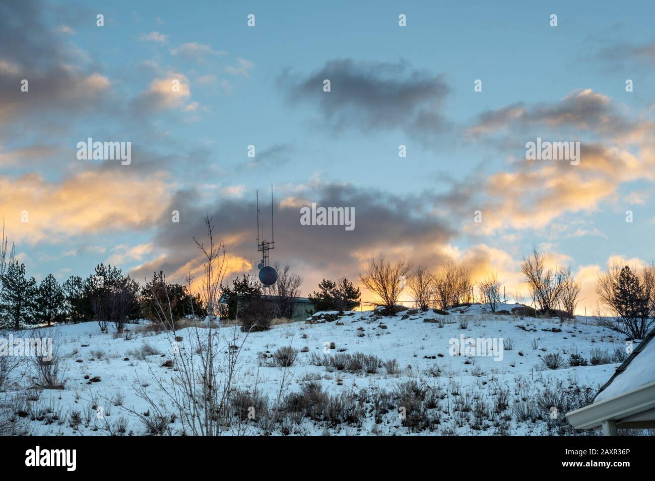 Clouds are illuminated from below under a colorful sky with a TV or satellite dish and antennae on top of a snow covered hill. Stock Photo