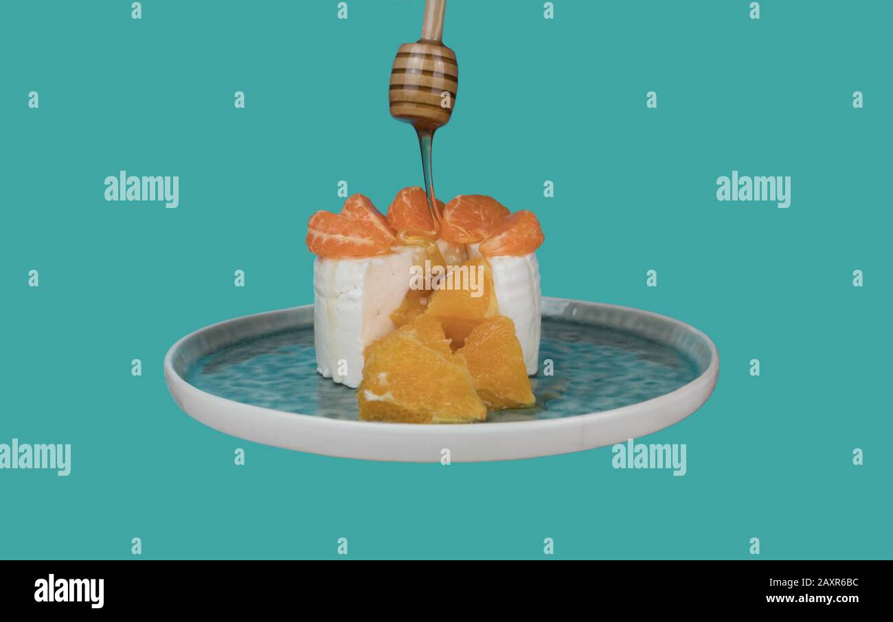 Fresh goat cheese with pieces of orange and honey that falls on top, on a cyan background Stock Photo