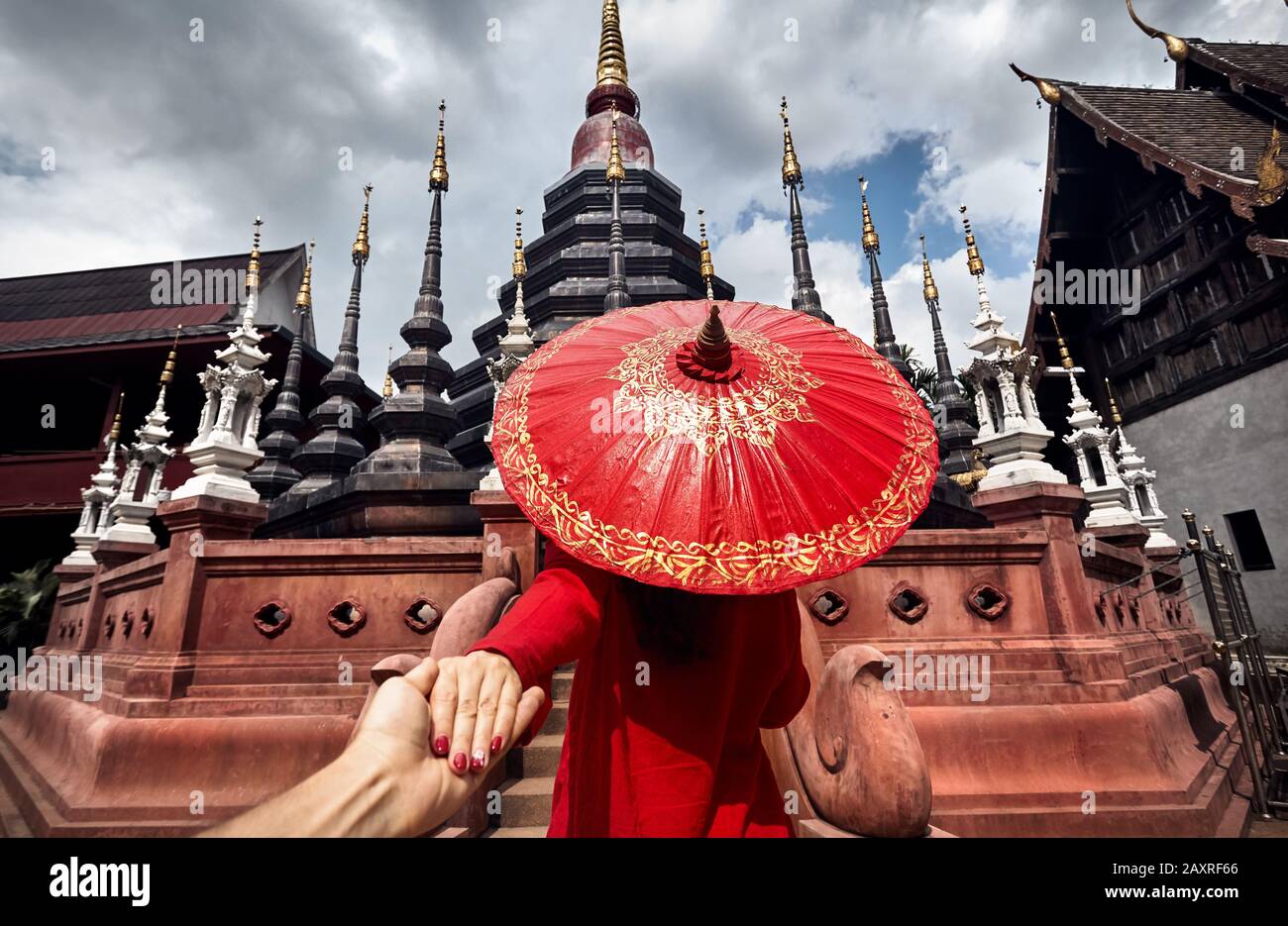 Woman with red traditional Thai umbrella holding man by hand and going to Black temple Wat Phan Tao in Chiang Mai, Thailand Stock Photo