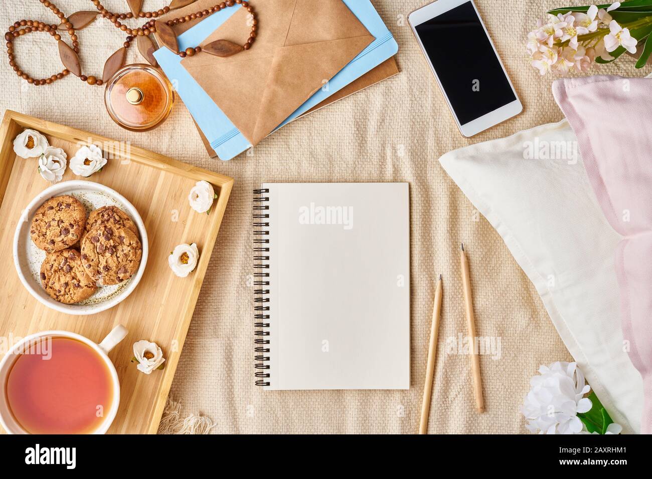 Mockup with notepad on bed and women's accessories, tea, cookies, pillows, flowers, letter, notebook. Cozy women's creative world. . Stock Photo
