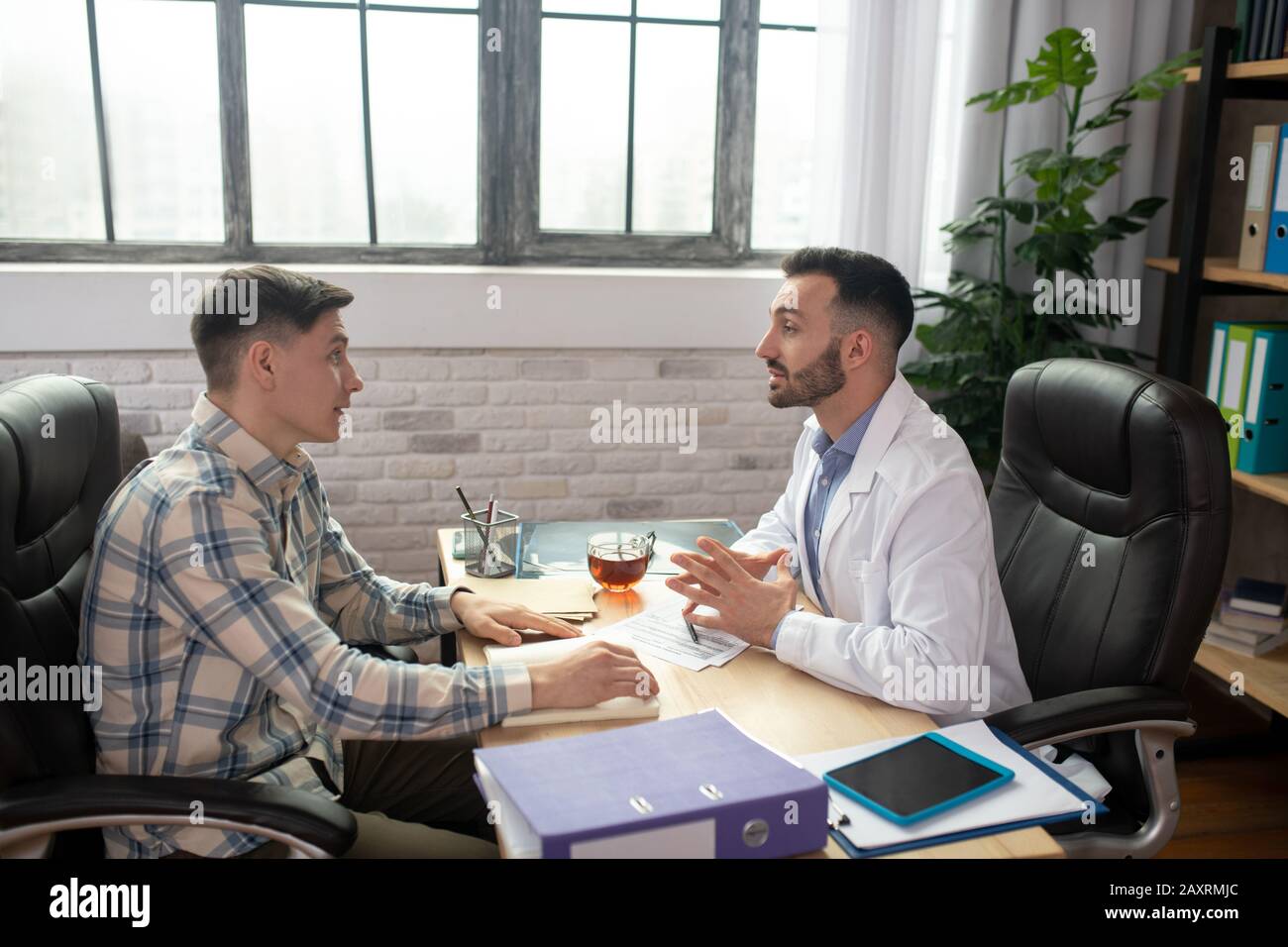Patient in checkered shirt explaining his problems to the doctor Stock Photo