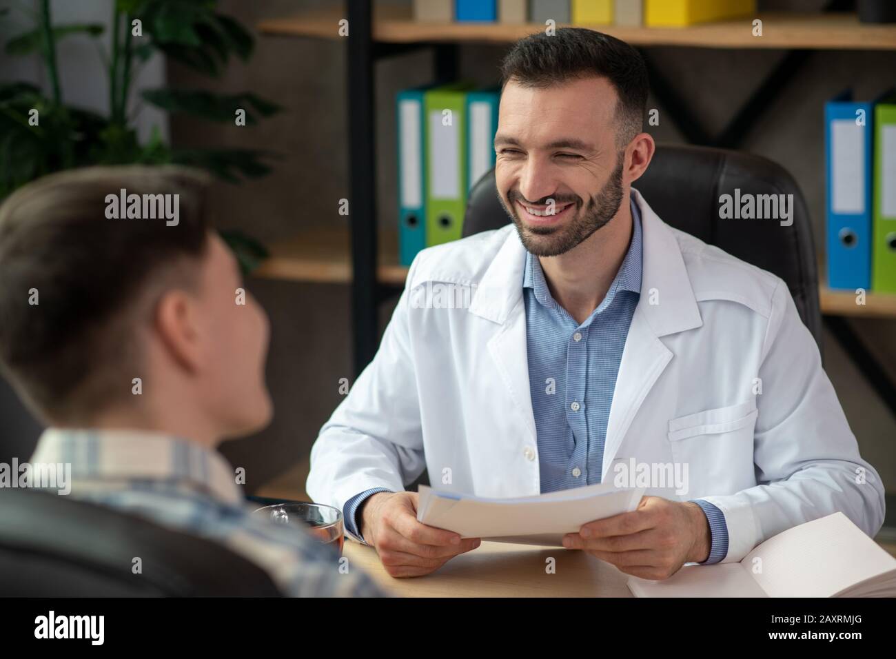 Dark-haired young doctor smiling friendly to his patient Stock Photo