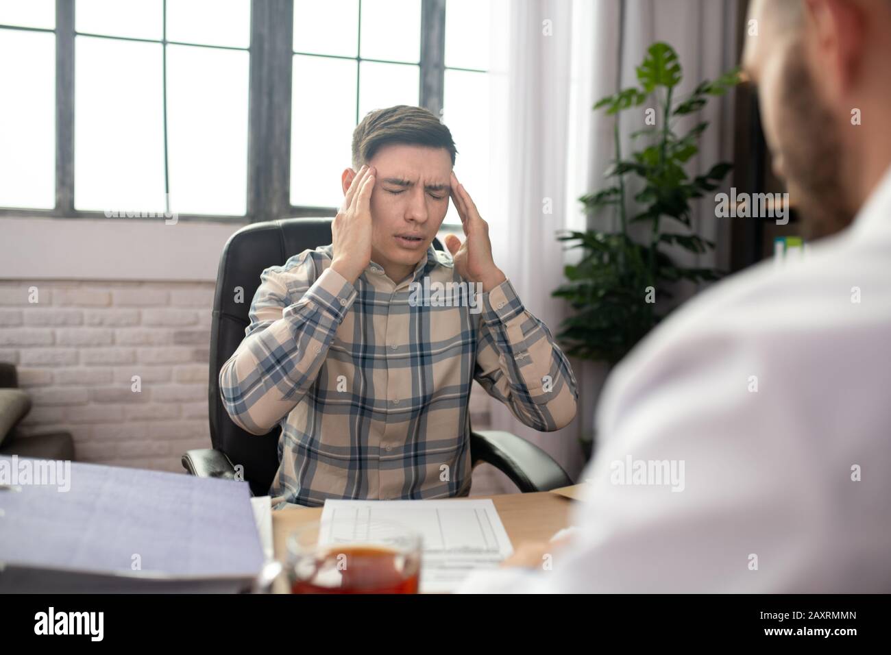 Patient in checkered shirt touching his head and complaining to the doctor Stock Photo