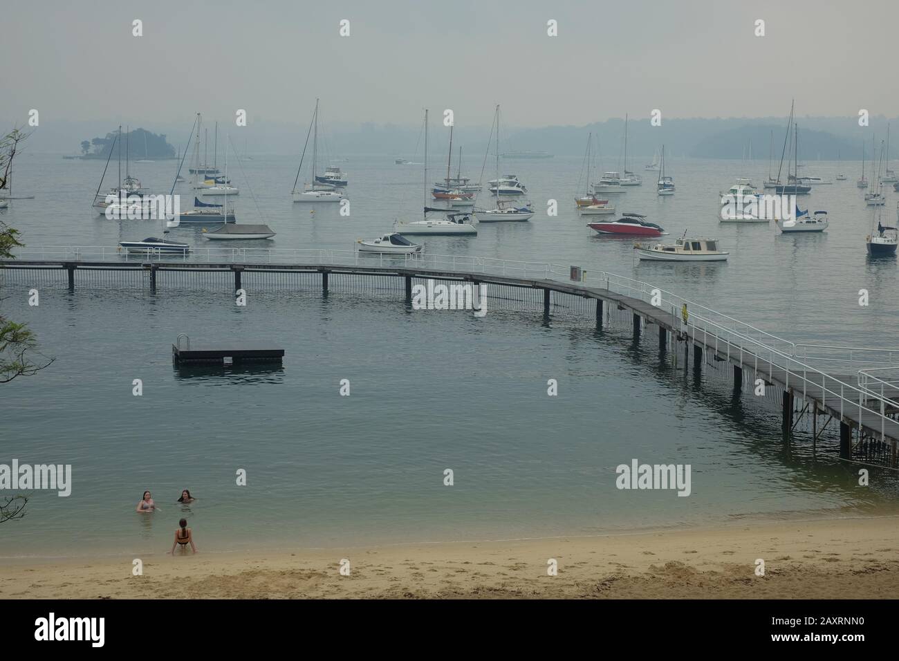 Climate Change - Three young women swim at Murray Rose Pool during the Australian bushfire crisis as smoke haze hangs over beach and Sydney Harbour Stock Photo