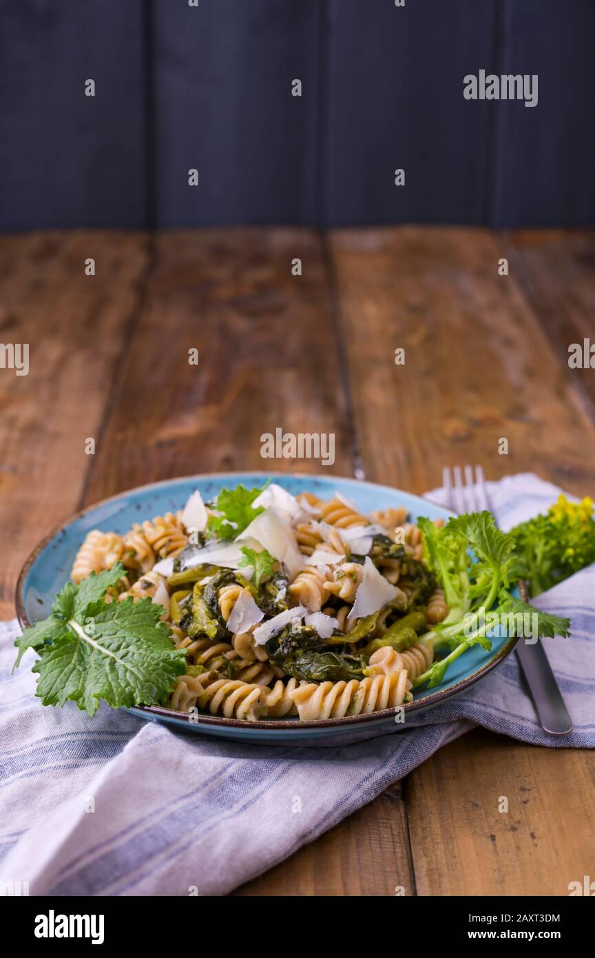 Cime di rapa pasta in a plate on with parmesan on a wooden table. Traditional food of the south of Italy, from Puglia. Rustic style photo.  Stock Photo