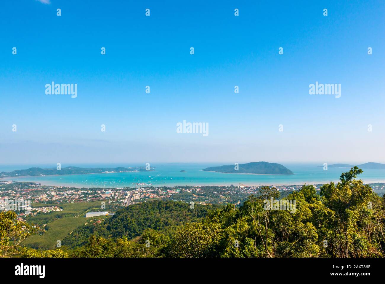 Nakkerd Hill, Phuket/Thailand-15December2019: Big Buddha hilltop viewpoint, trees in the foreground and the sea and cityscape in the background on a b Stock Photo