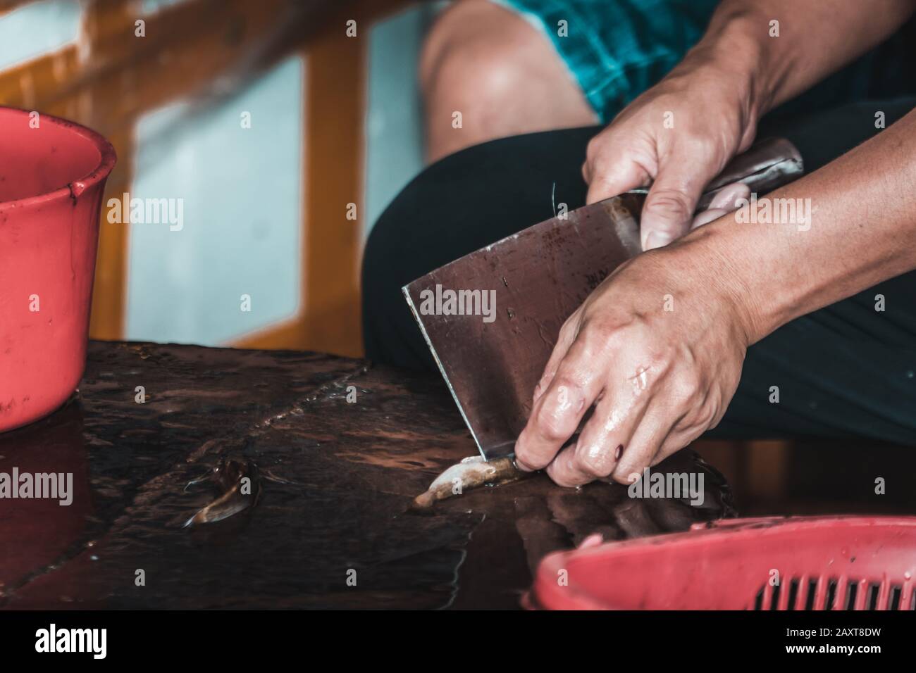 Close up of hands of a chinese person peeling scales off small fish on
