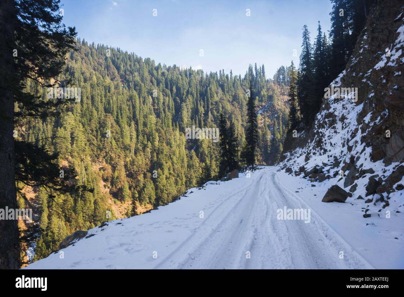 A snow-covered road with tyre tread marks on the dark side of the mountain. Stock Photo