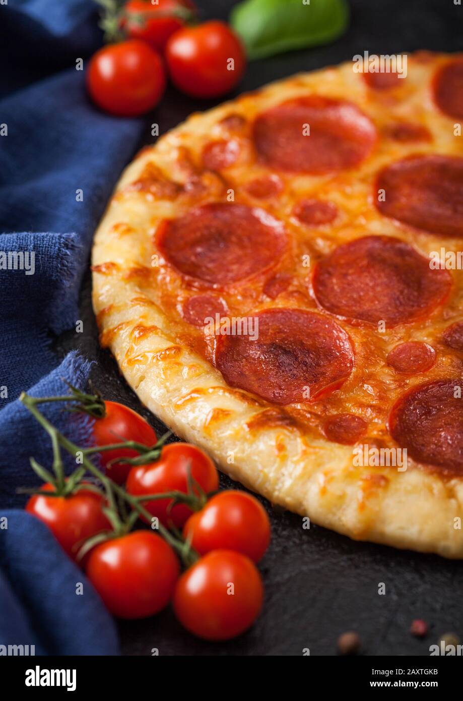 Fresh round baked Pepperoni italian pizza with tomatoes with basil on black kitchen table