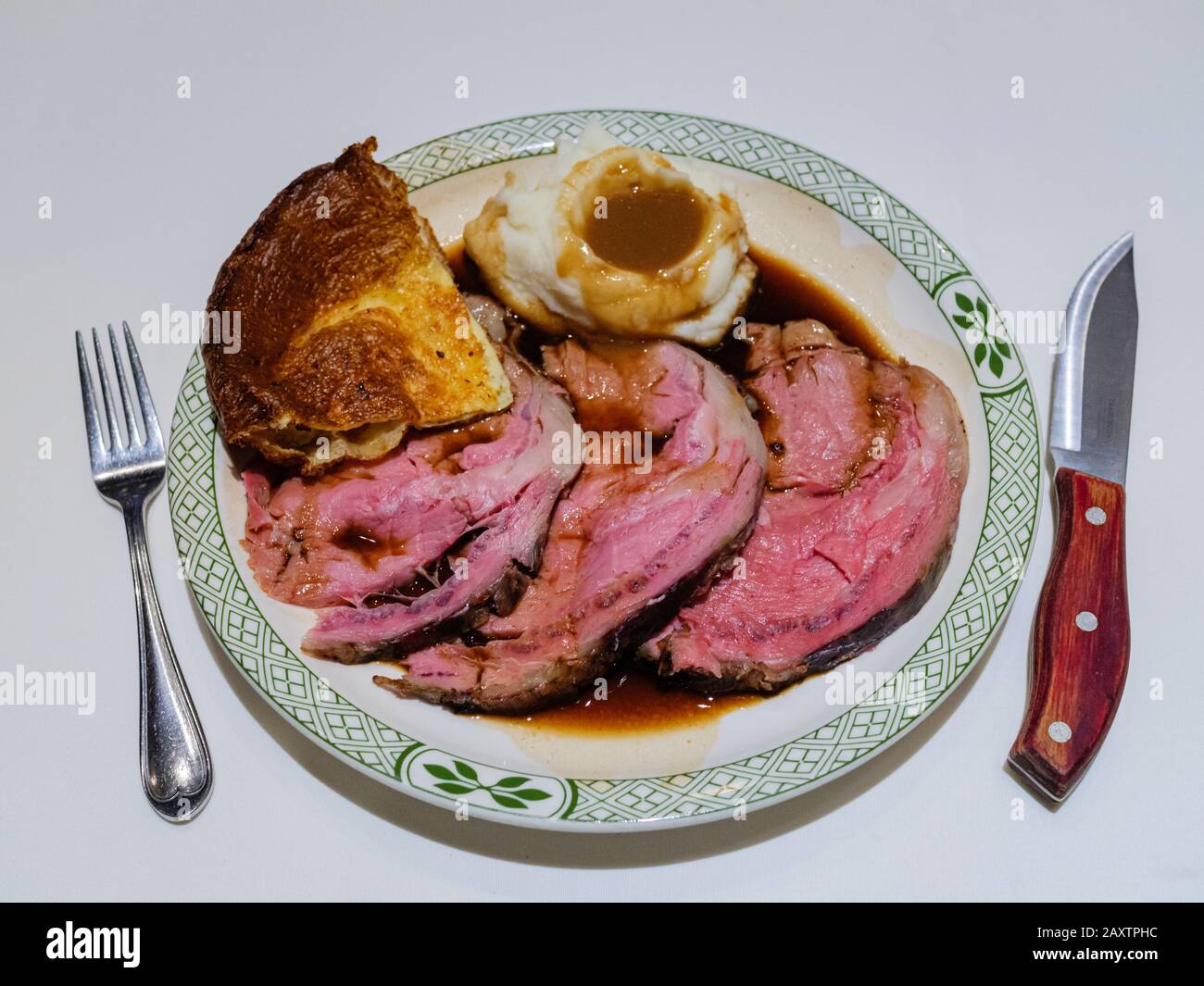 A delicious traditional Sunday roast dinner - slices of medium-rare roast beef and gravy, mashed potato, and Yorkshire pudding on a porcelain plate Stock Photo