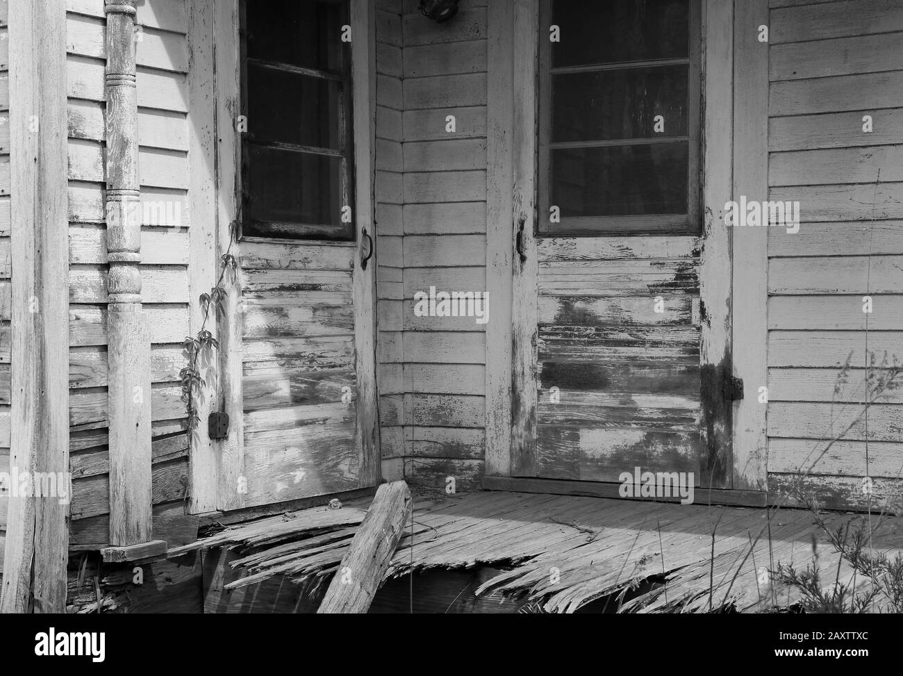 Grayscale shot of an abandoned farmhouse porch in dilapidated condition Stock Photo