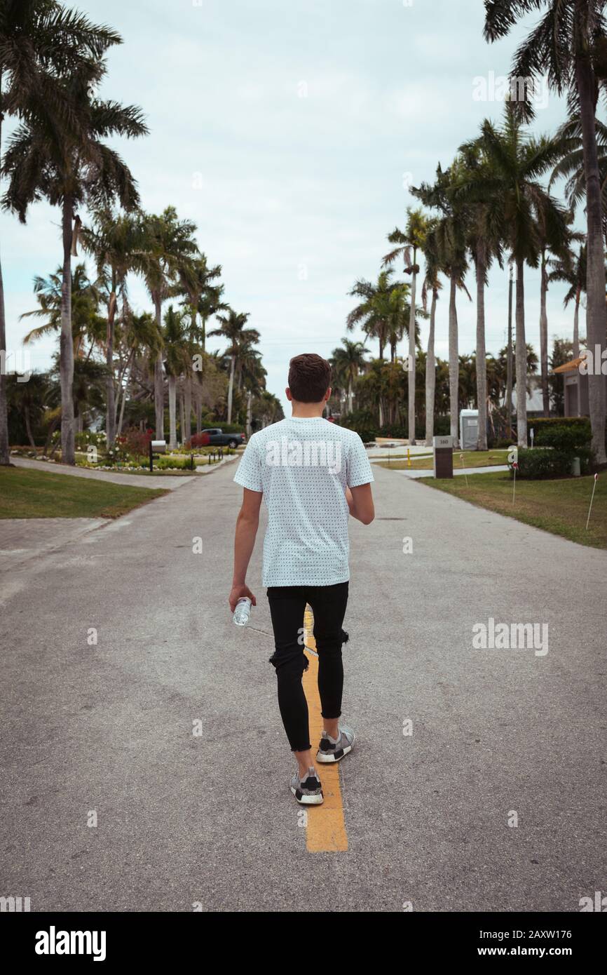 Teenager boy walking in the middle of the road with palm trees and