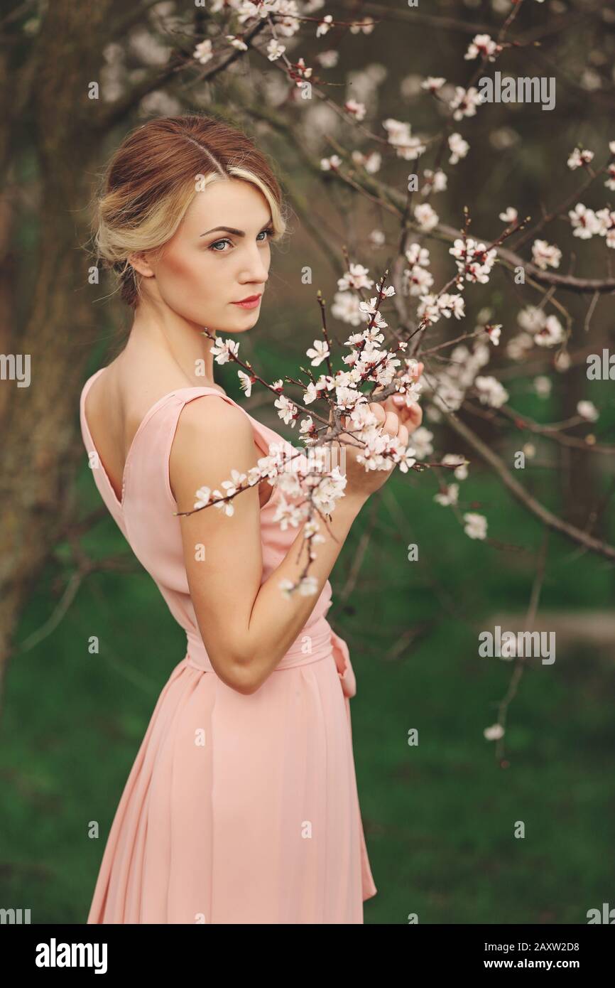young stylish woman near blossoming tree in spring park. blonde girl with  hairstyle in pink dress. concept of women's day Stock Photo - Alamy
