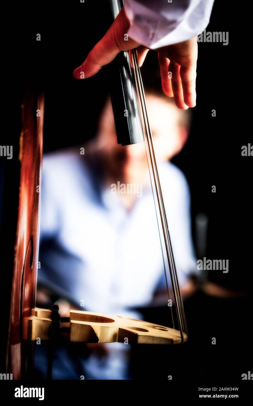 Arty image of double bass player's hand about to pluck strings, neck and bridge. Shallow depth of field with soft focus drummer black background Stock Photo