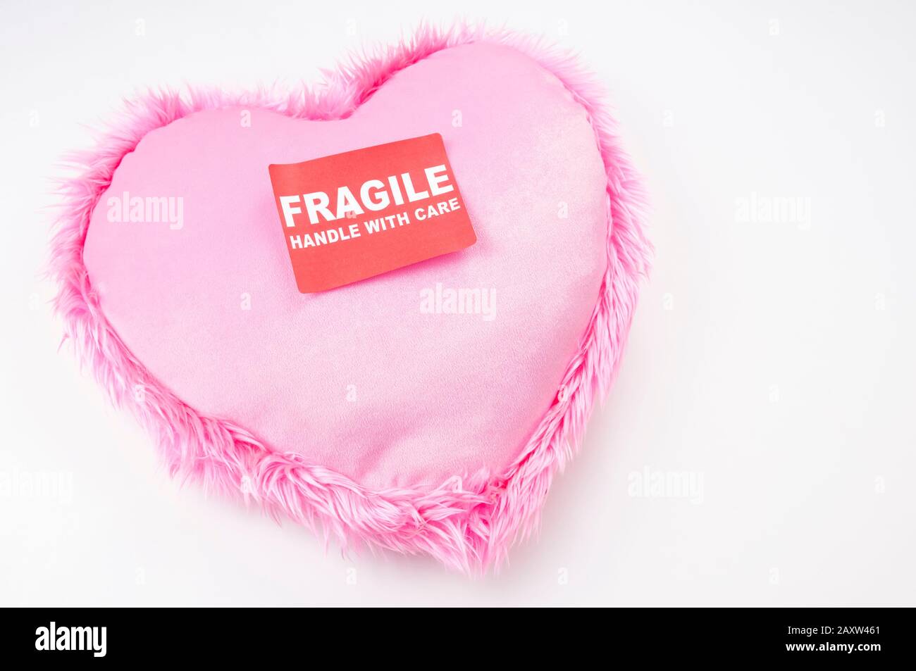 Pink heart with furry trim sitting with a Fragile Handle With Care sticker on white background Stock Photo