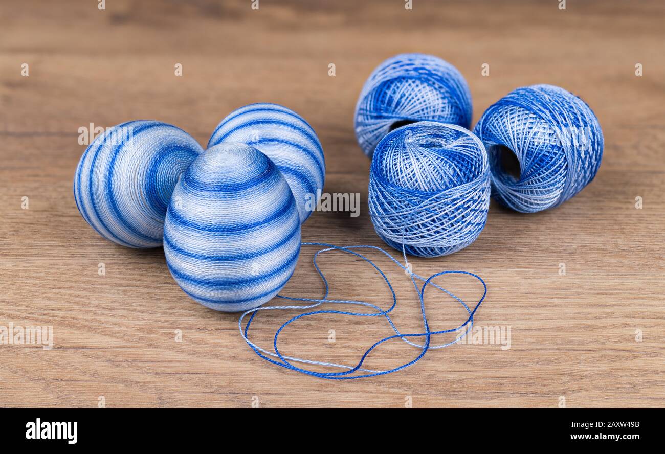 Blue striped Easter eggs and cotton yarn in decorative skeins on wooden background. Group of streaked decorated egg shells and hanks of sewing thread. Stock Photo