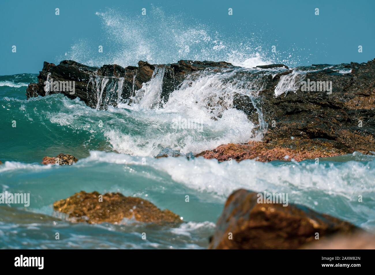 Waves crashing on rocks close-up under the bright sun Stock Photo