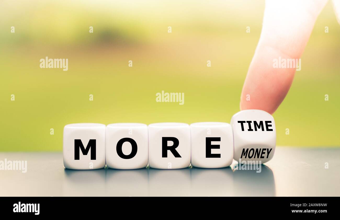 Hand turns dice and changes the expression 'more money' to 'more time'. Stock Photo