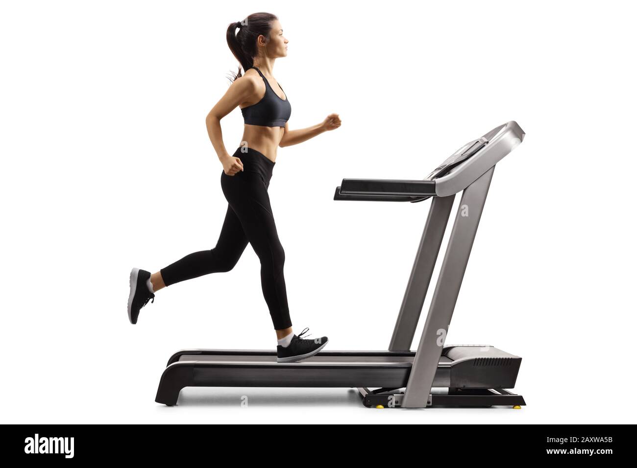 Full length profile shot of a young female in black leggings running on a treadmill isolated on white background Stock Photo