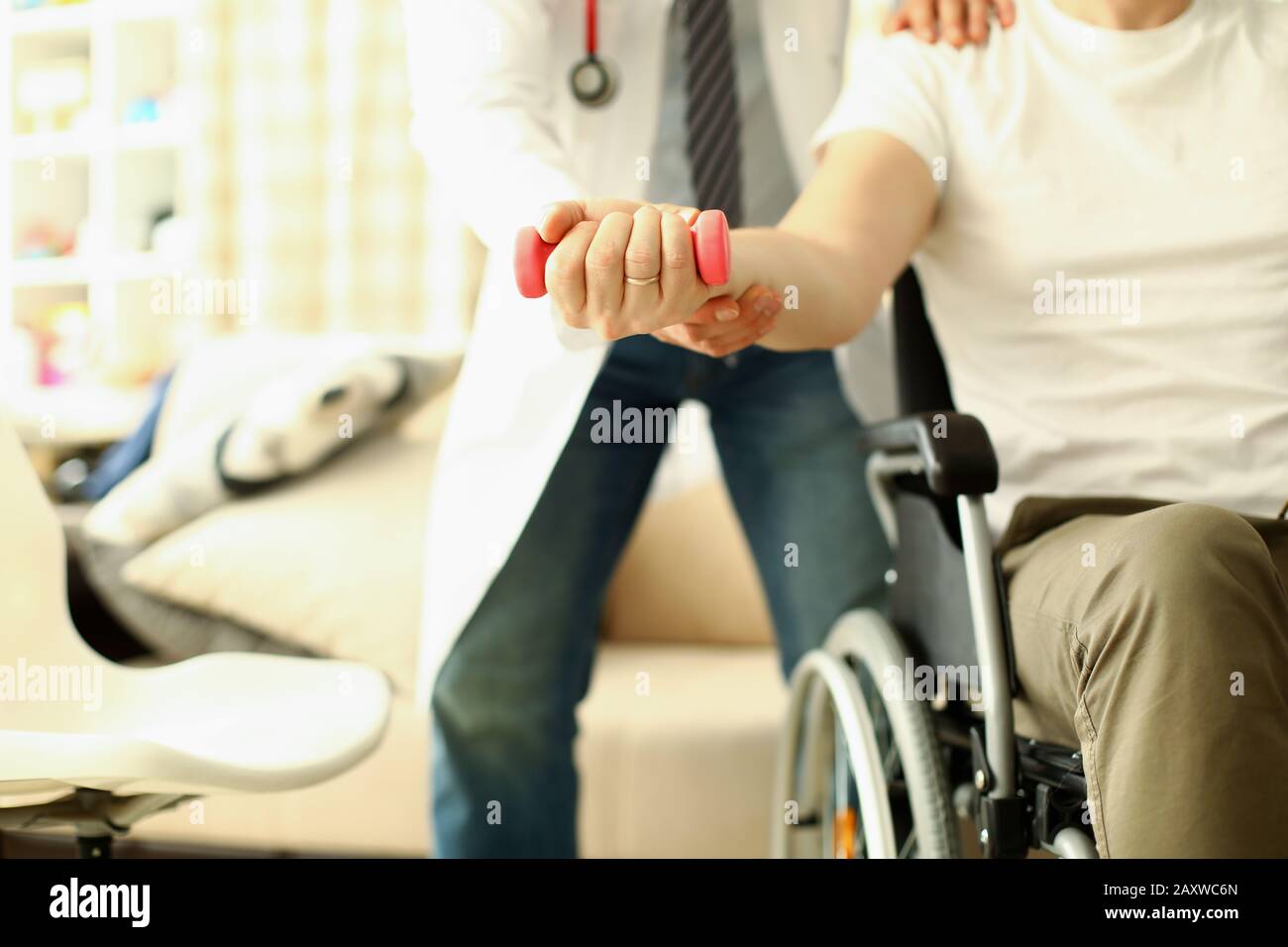 Male doctor helps lift dumbbell to disabled patient rehabilitation therapy concept. Stock Photo