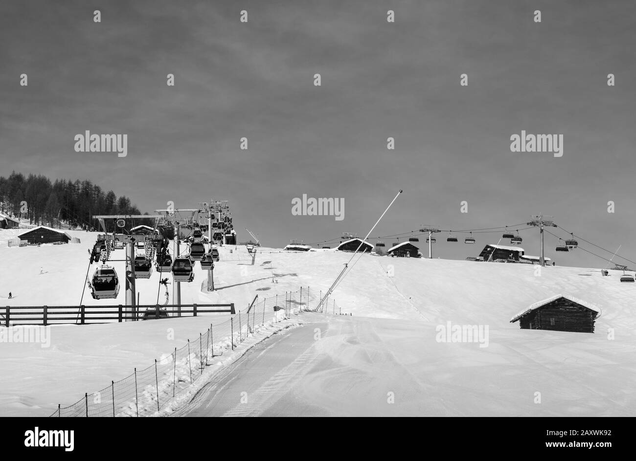 Black and white snowy ski track prepared with snow grooming machine, gondola lift, chair-lift, snow cannons at ski resort. Mountains in winter. Italia Stock Photo