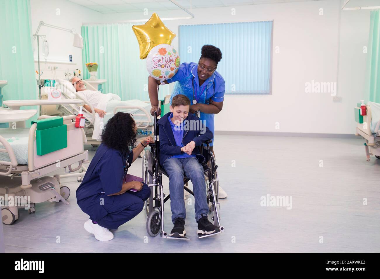 Doctor and nurse pushing boy patient in wheelchair in hospital ward Stock Photo