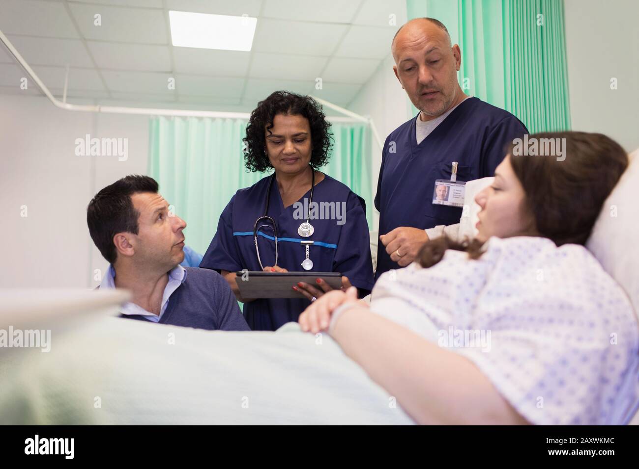 Doctors making rounds, talking with couple in hospital room Stock Photo