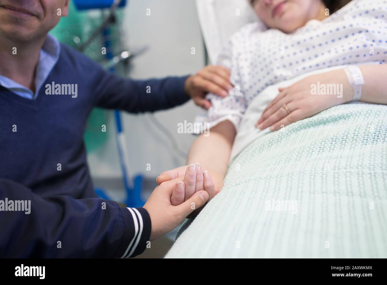 Affectionate son holding hands with mother resting in hospital bed Stock Photo