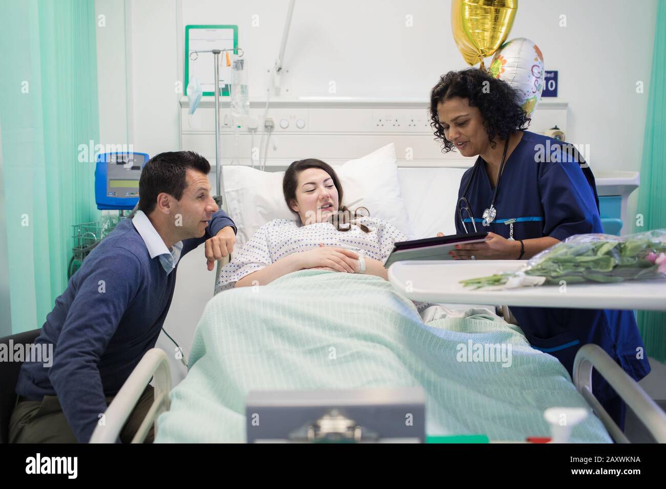 Doctor with digital tablet making rounds, talking with couple in hospital room Stock Photo
