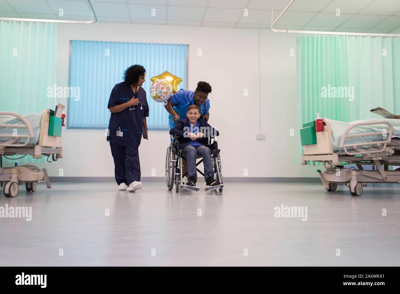 Doctor and nurse pushing boy patient in wheelchair in hospital ward Stock Photo