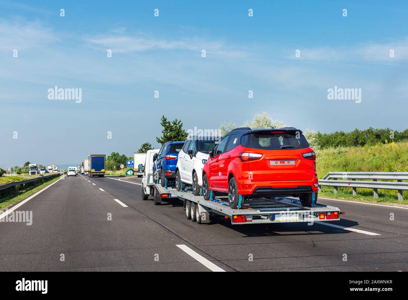Car carrier trailer with new blue white and red car on the highway Stock Photo