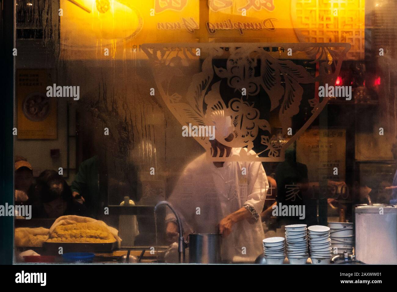Hong Kong - November, 2019:  Window of Chinese restaurant showing chef cooking food and people eating Stock Photo