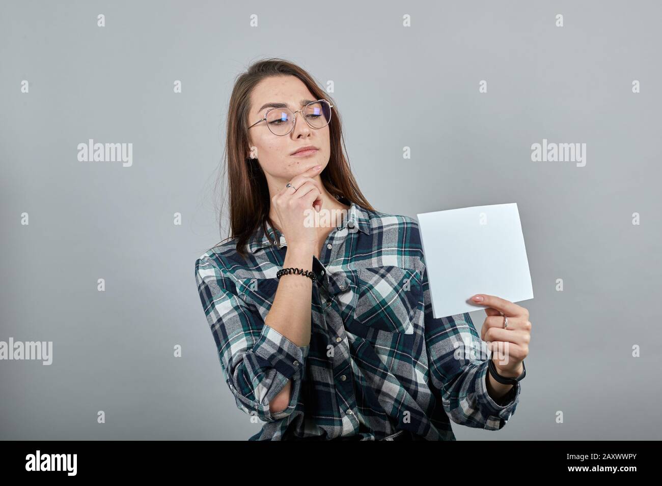 on grey background smart woman with glasses thinks, holds her chin with hand Stock Photo