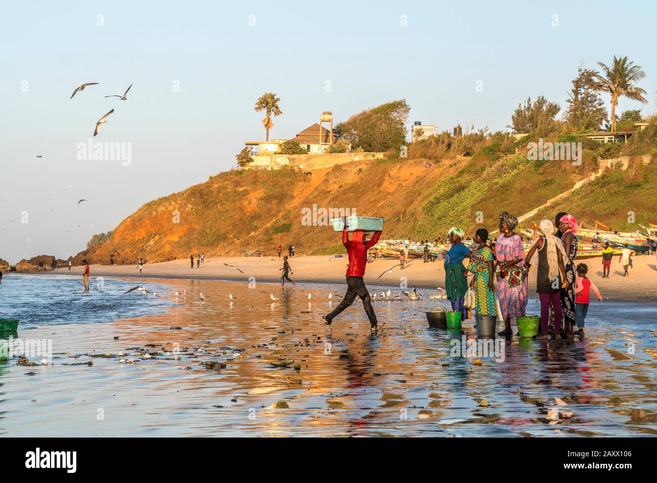 Women in colorful traditional clothes wait to collect fish from boat on  beach Bakau The Gambia Stock Photo - Alamy