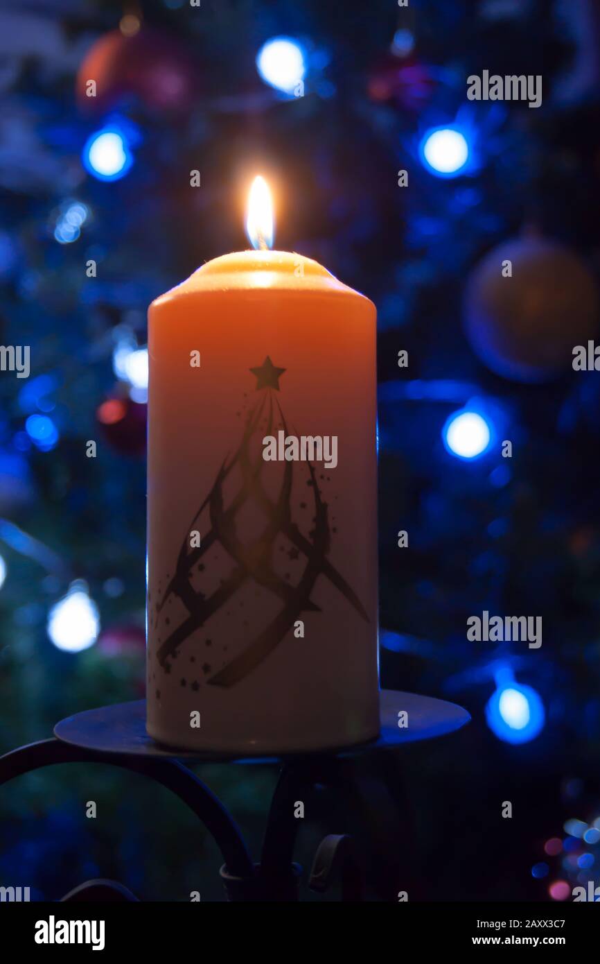 A large candle burns against the background of a garland with shining lights. Vertical photo, defocus. Mystic esoteric romance divination mood christening Christmas carol setcers Stock Photo