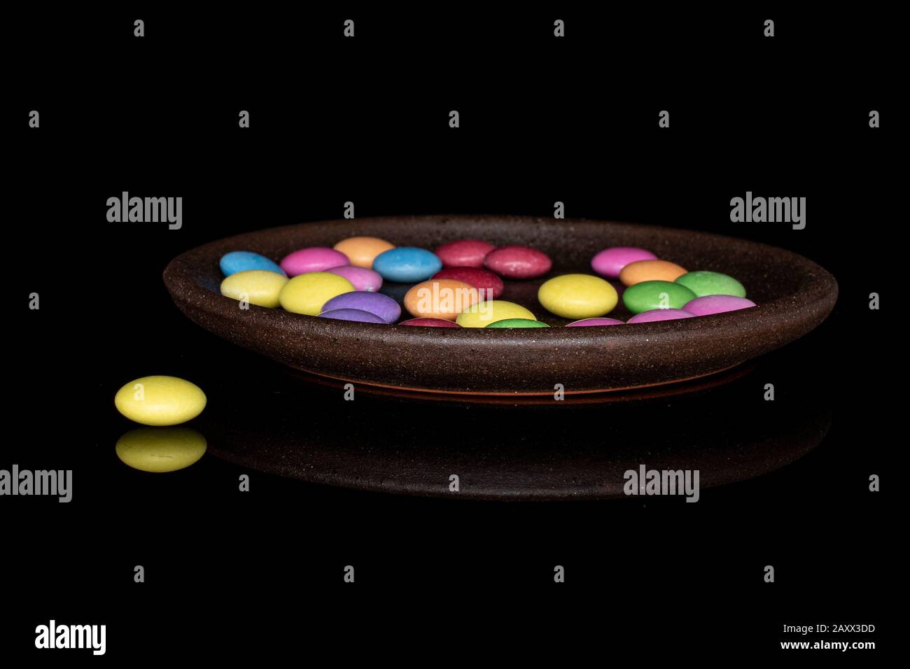 Lot of whole sweet colourful candy with brown ceramic coaster isolated on black glass Stock Photo