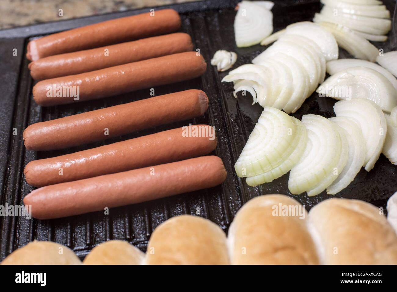 Cooking hot dogs on a griddle with sliced onion, smoked Wiener sausages