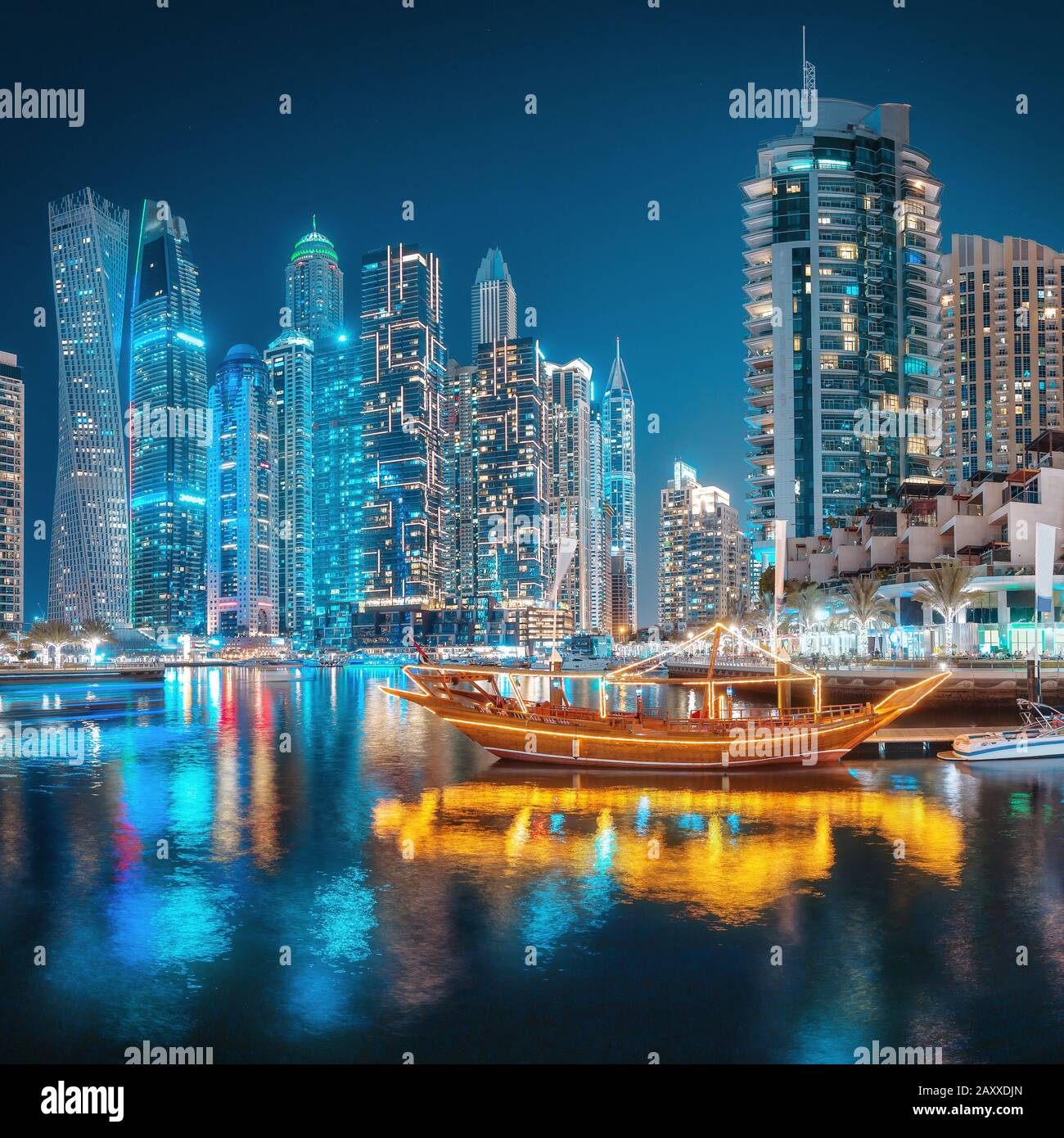 Multicolored lights of the night city in the Dubai Marina district. Stylized ancient Arabic ship Abra Dhow with lights in the foreground. Stock Photo