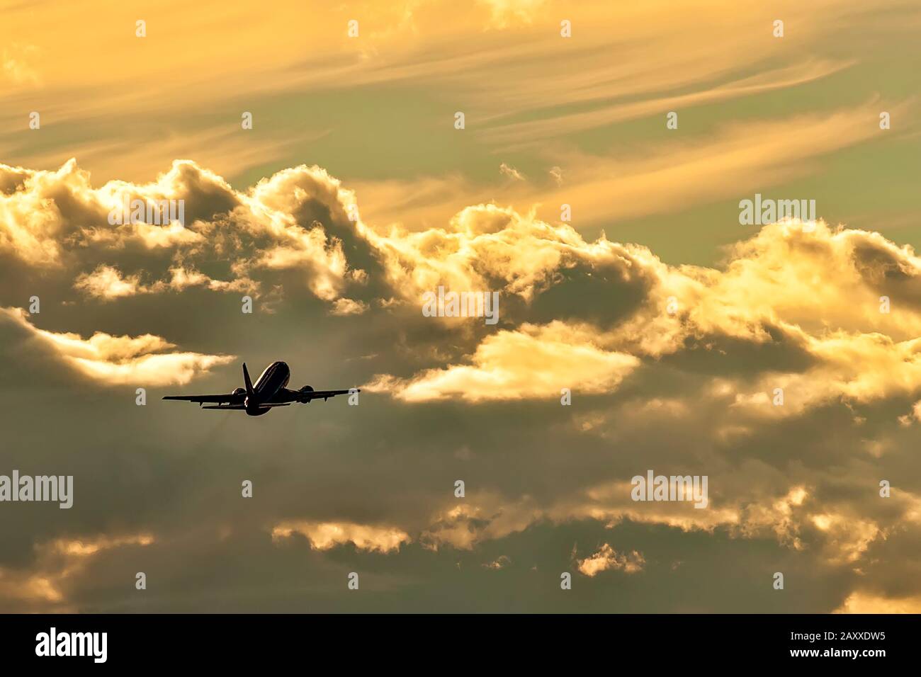 Silhouette of jet airplane flying towards the clouds at sunset. Stock Photo