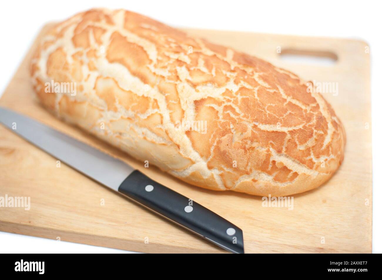 Freshly baked uncut loaf of crusty white bread on a bread board with a bread knife isolated on white Stock Photo