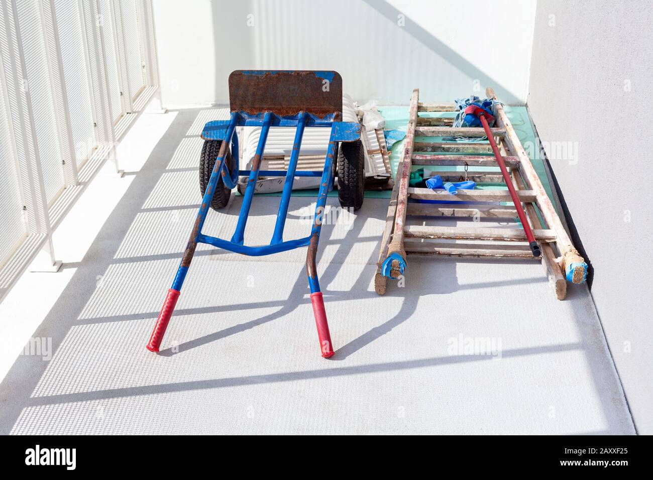 Handtruck and a wooden painter ladder and a mop laying on the white balcony. House or flat under construction abstract concept. Construction job Stock Photo