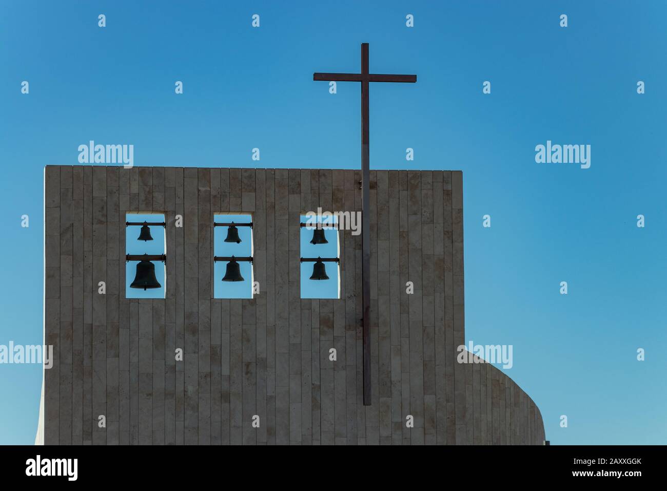 Cross on church over clear blue sky. Six bells of different sizes on