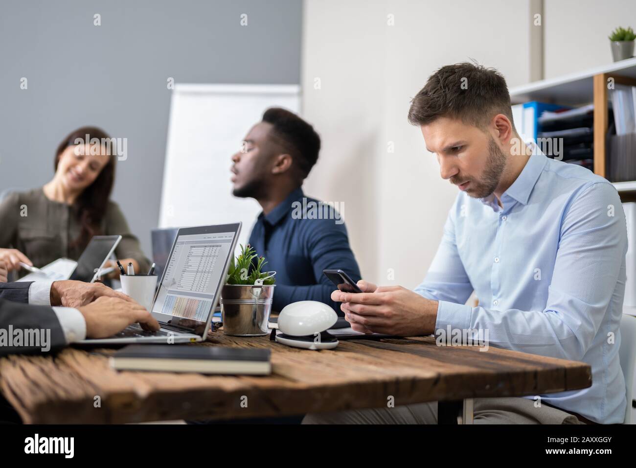 Distracted Businessman Using Mobile Phone In Meeting Stock Photo