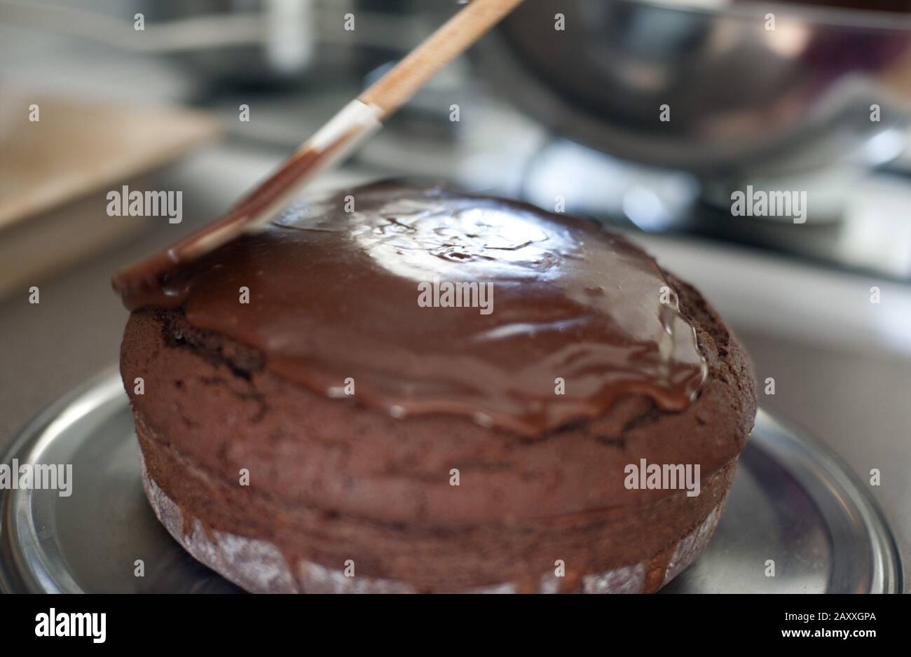 Cook spreading chocolate icing onto a freshly baked cake in a kitchen with a wooden spatula Stock Photo