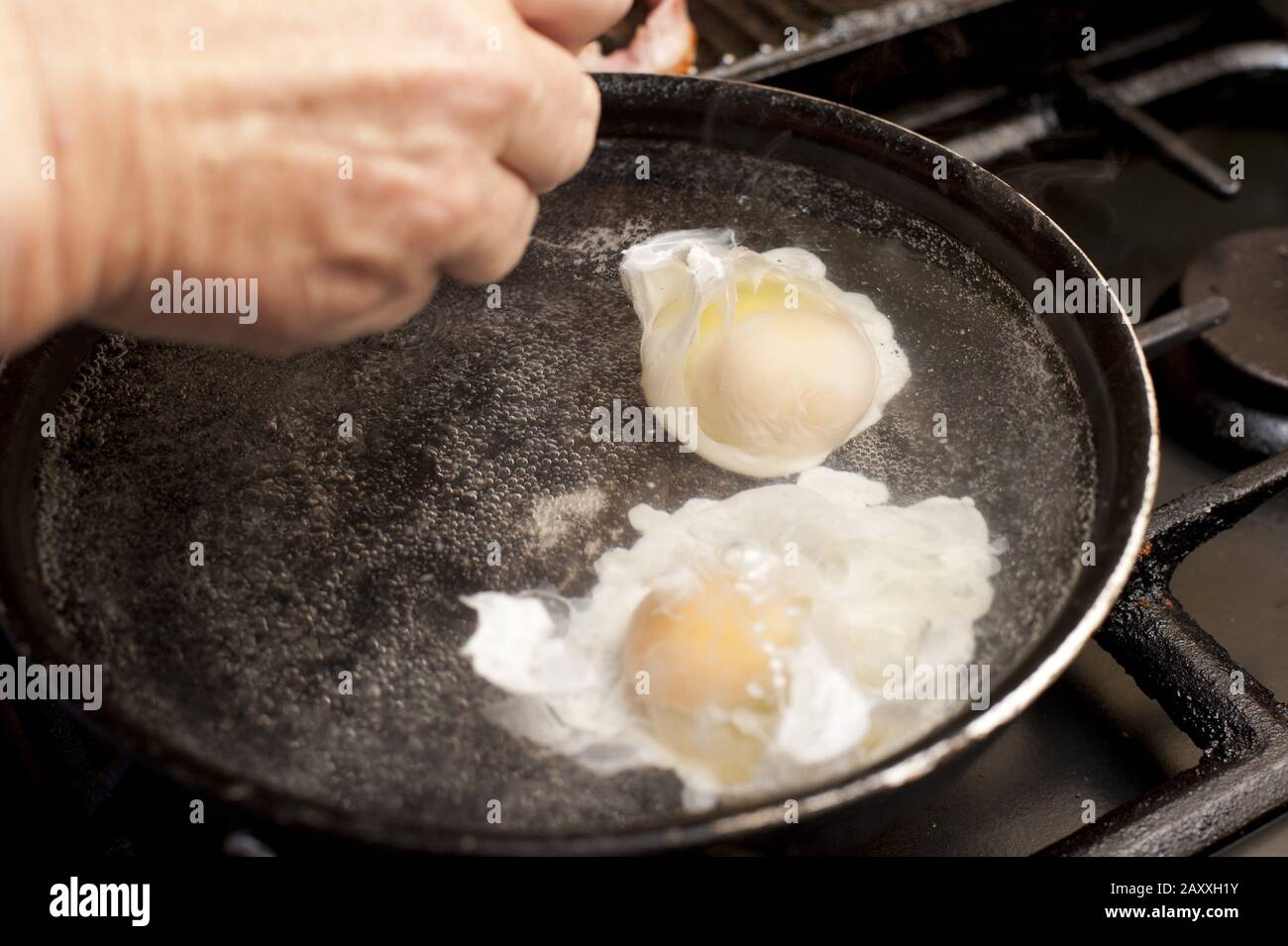 Overhead view of hands preparing two eggs in boiling water set on a gas